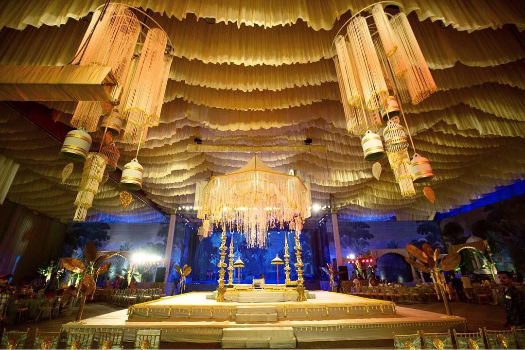 Gold-draped reception ceiling with chandeliers and blue uplighting by RAW Group